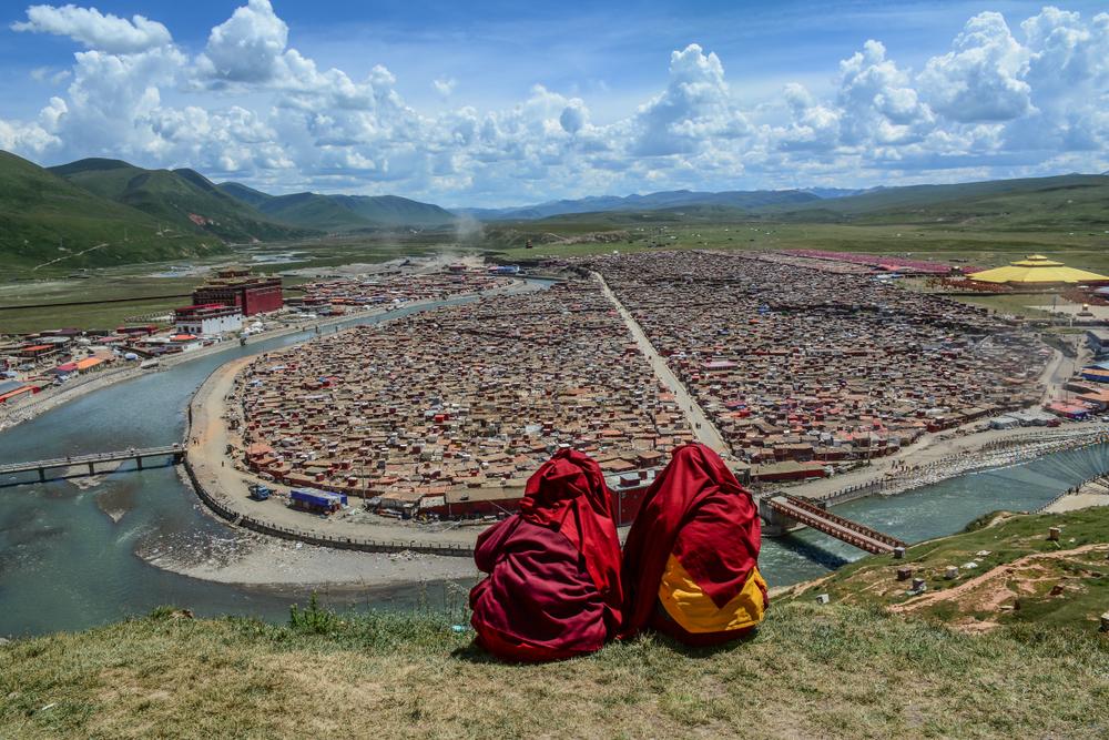 Tibetan monks sitting on the hill and looking at Yarchen Gar Tibetan Buddhist monastery in Sichuan, China. (Phuong D. Nguyen/Shutterstock)