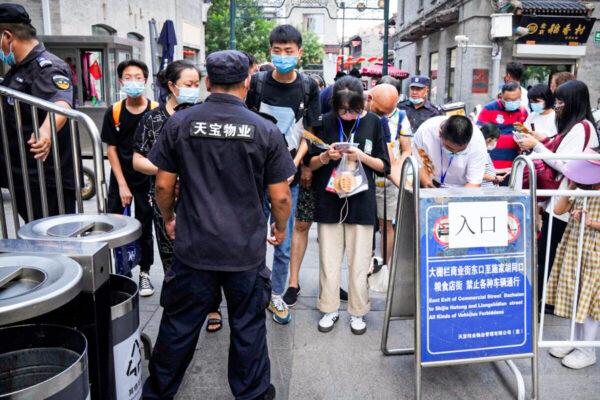 A security guard checks health codes on people’s smartphones at a tourist shopping street in Beijing, on Aug. 3, 2021. (Mark Schiefelbein/AP Photo)