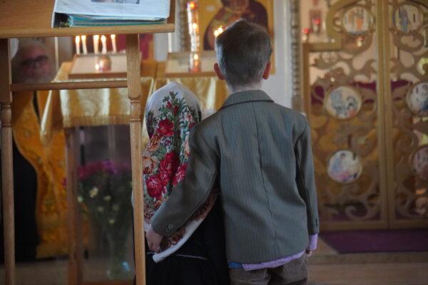 A young boy with his arm around a young girl during the Sunday morning liturgy service at Holy Archangels Orthodox Church in Phoenix, Ariz., on March 6. Below, the boy's mother helps him light a candle. (Allan Stein/The Epoch Times)