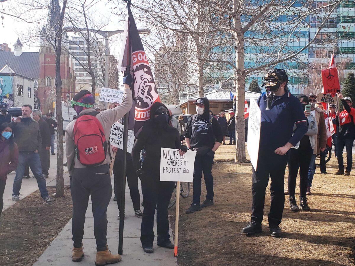 Counter-protesters carry flags and signs displaying messages in opposition to a protest by demonstrators who are against government COVID-19 mandates, at a rally at Central Memorial Park in the Beltline neighbourhood of Calgary on March 19, 2022. (Michael Wing/The Epoch Times)