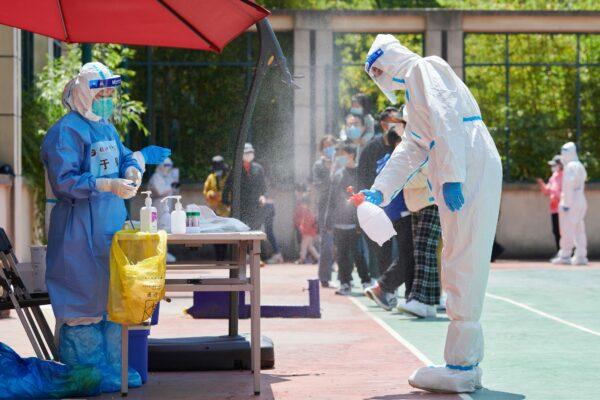 A community volunteer wearing protective equipment disinfects an area where swabs are taken from residents for COVID-19 in a compound during a lockdown in Pudong district, Shanghai, on April 17, 2022. (Liu Jin/AFP via Getty Images)