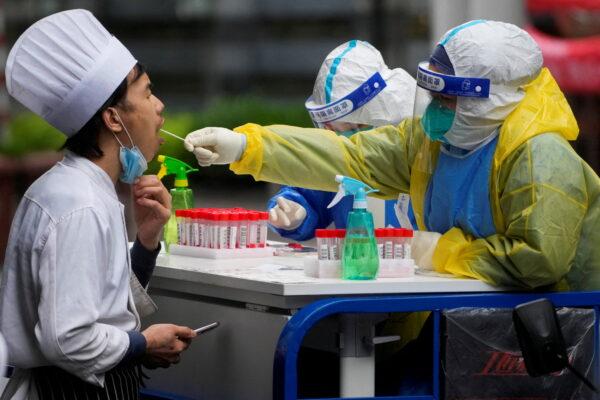 A medical worker in protective gear collects a swab sample from a chef for nucleic acid testing, during a lockdown in Shanghai, China, May 13, 2022. (Aly Song/Reuters)