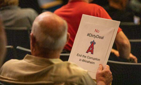 A man attends an Anaheim City Council meeting while holding a sign criticizing Anaheim's Angels Stadium deal in Anaheim, Calif., on May 24, 2022. (John Fredricks/The Epoch Times)