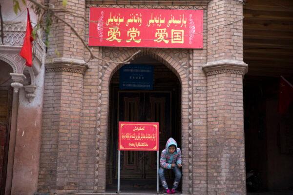A child rests near the entrance to the mosque where a banner in red reads "Love the Party, Love the country" in the old city district of Kashgar in western China's Xinjiang region, Nov. 4, 2017. (AP Photo/Ng Han Guan)