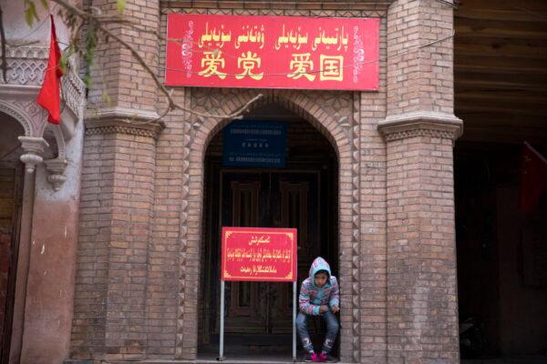 A child rests near the entrance to the mosque where a banner in red reads "Love the Party, Love the country" in the old city district of Kashgar in western China's Xinjiang region, Nov. 4, 2017.  (AP Photo/Ng Han Guan)