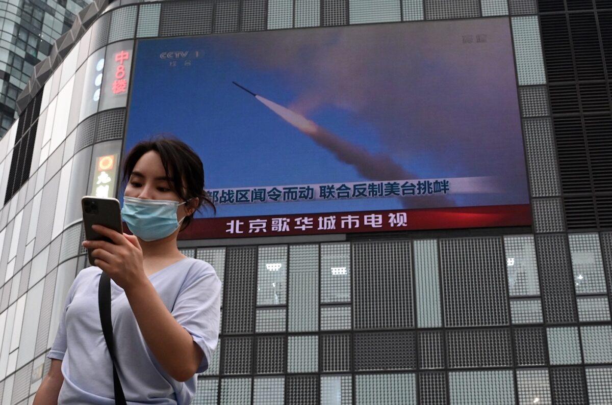 A woman uses her mobile phone as she walks in front of a large screen showing a news broadcast about China's military exercises encircling Taiwan, in Beijing, on Aug. 4, 2022. (Noel Celis/AFP via Getty Images)