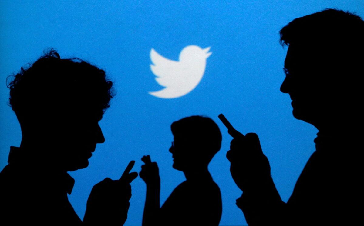 People holding mobile phones are silhouetted against a backdrop projected with the Twitter logo in this illustration picture taken on Sept. 27, 2013. (Kacper Pempel/Illustration/Reuters)