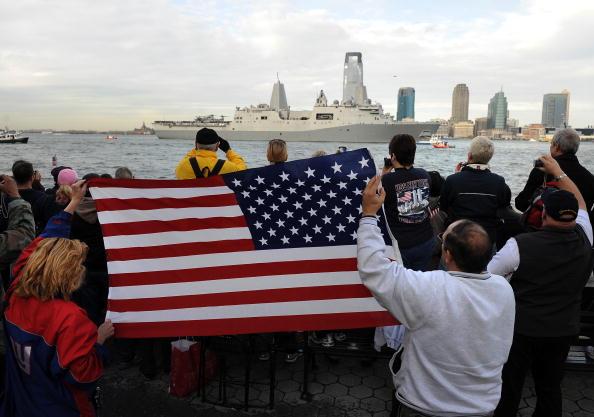 People wave an American flag as an American ship enters New York harbor. The author says that the U.S. Navy made the world safe for trade. (Stan Honda/AFP/via Getty Images)