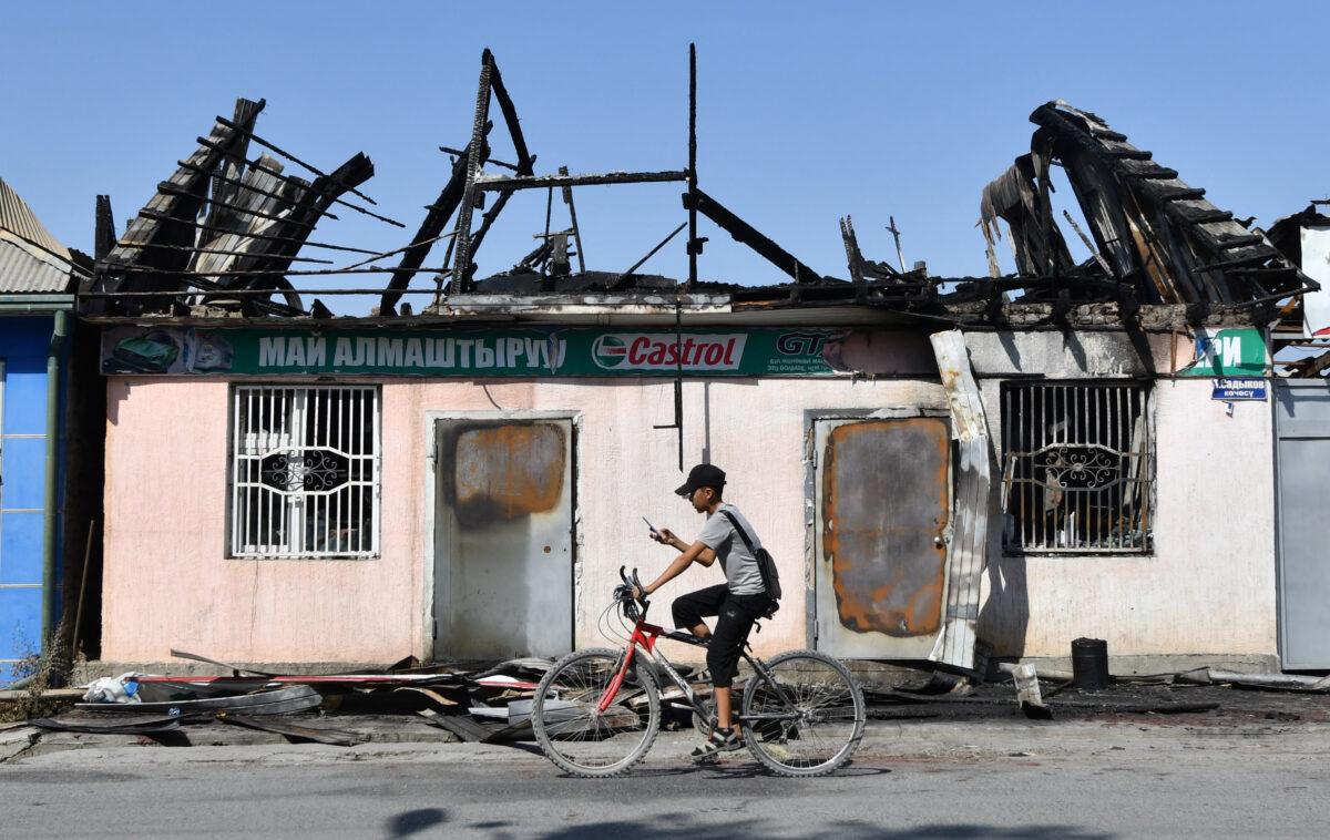 A boy rides his bicycle past a burned-out auto oil store in Batken, some 1000 kilometres from Bishkek, on Sept. 22, 2022. (Vyacheslav Oseledko/AFP via Getty Images)