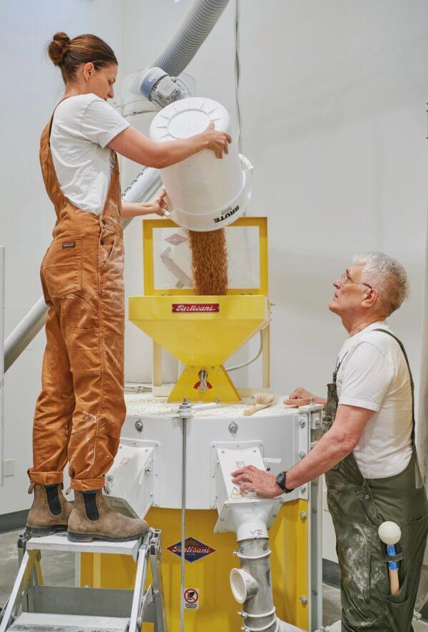 Emma and Jeff Zimmerman fill the mill with einkorn to make flour. The stone is encased by the white metal cover. (David Alvarado)