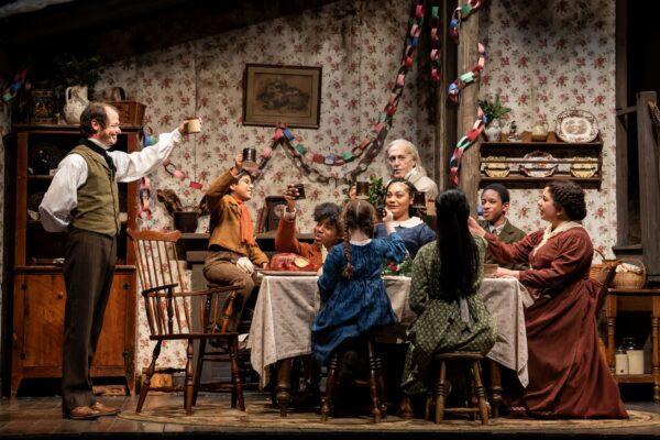 (L–R) Bob Cratchit (Thomas J. Cox) makes a toast as Tiny Tim (Vikram Konkimalla), Peter Cratchit (Jalen Smith), Emily Cratchit (Presley Rose Jones), Fan (Ariana Burks), Ebenezer Scrooge (Larry Yando), Belinda Cratchit (Rika Nishikawa), Turkey Child (Amir Henderson), and Martha Cratchit (Susaan Jamshidi) look on, in “A Christmas Carol.” (Liz Lauren)