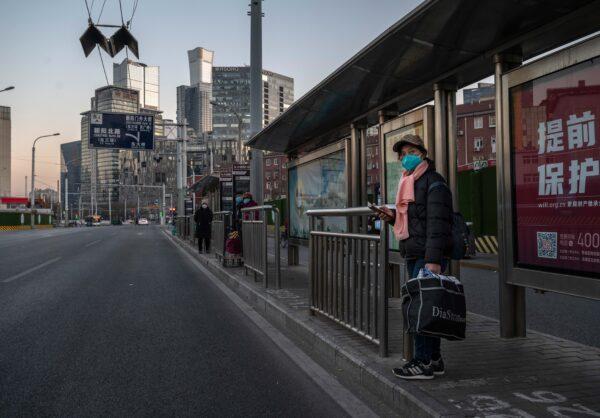 A woman wears a mask as she waits at a bus stop on a usually busy street in the central business district in Beijing on Dec. 6, 2022. (Kevin Frayer/Getty Images)