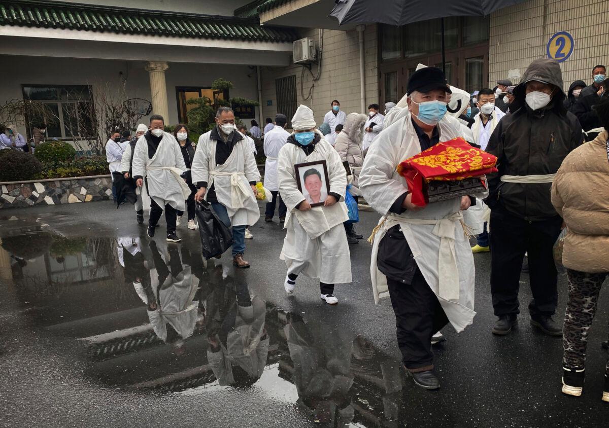A mourner carries the cremated remains of a loved one as he and others wear traditional white funeral clothing during a funeral in Shanghai, in a file photo. (Kevin Frayer/Getty Images)