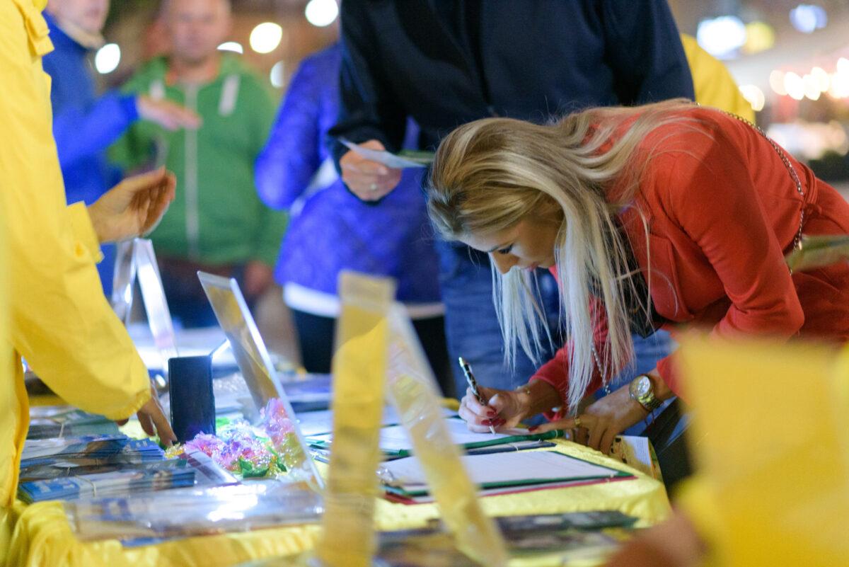 A woman signs a petition during a candlelight vigil held by Falun Dafa practitioners in the center of Warsaw, Poland, on Sept. 9, 2022. (Mihut Savu/The Epoch Times)