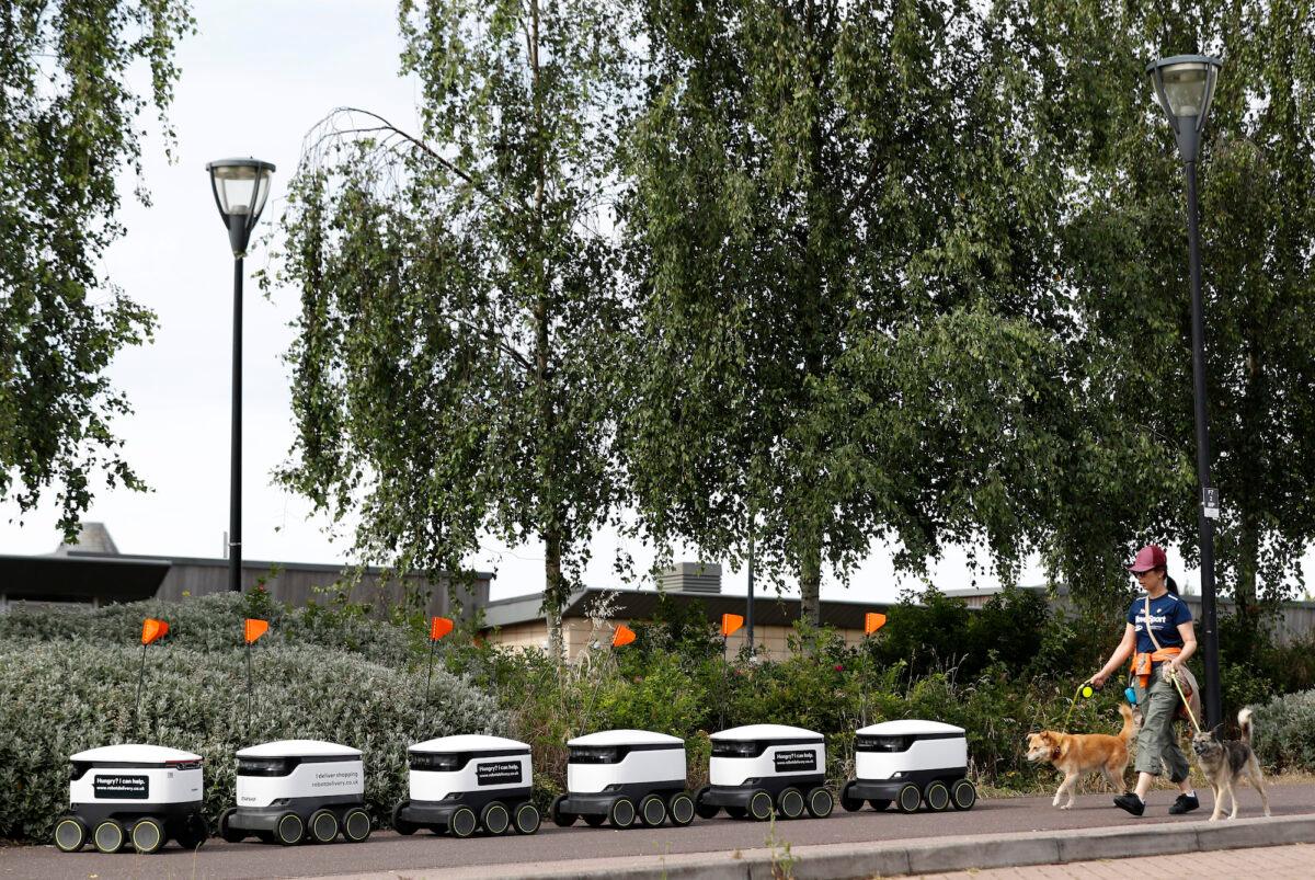 A woman walks her dogs past Starship delivery robots waiting for orders in Milton Keynes, England, on July 23, 2020. (Darren Staples/Getty Images)