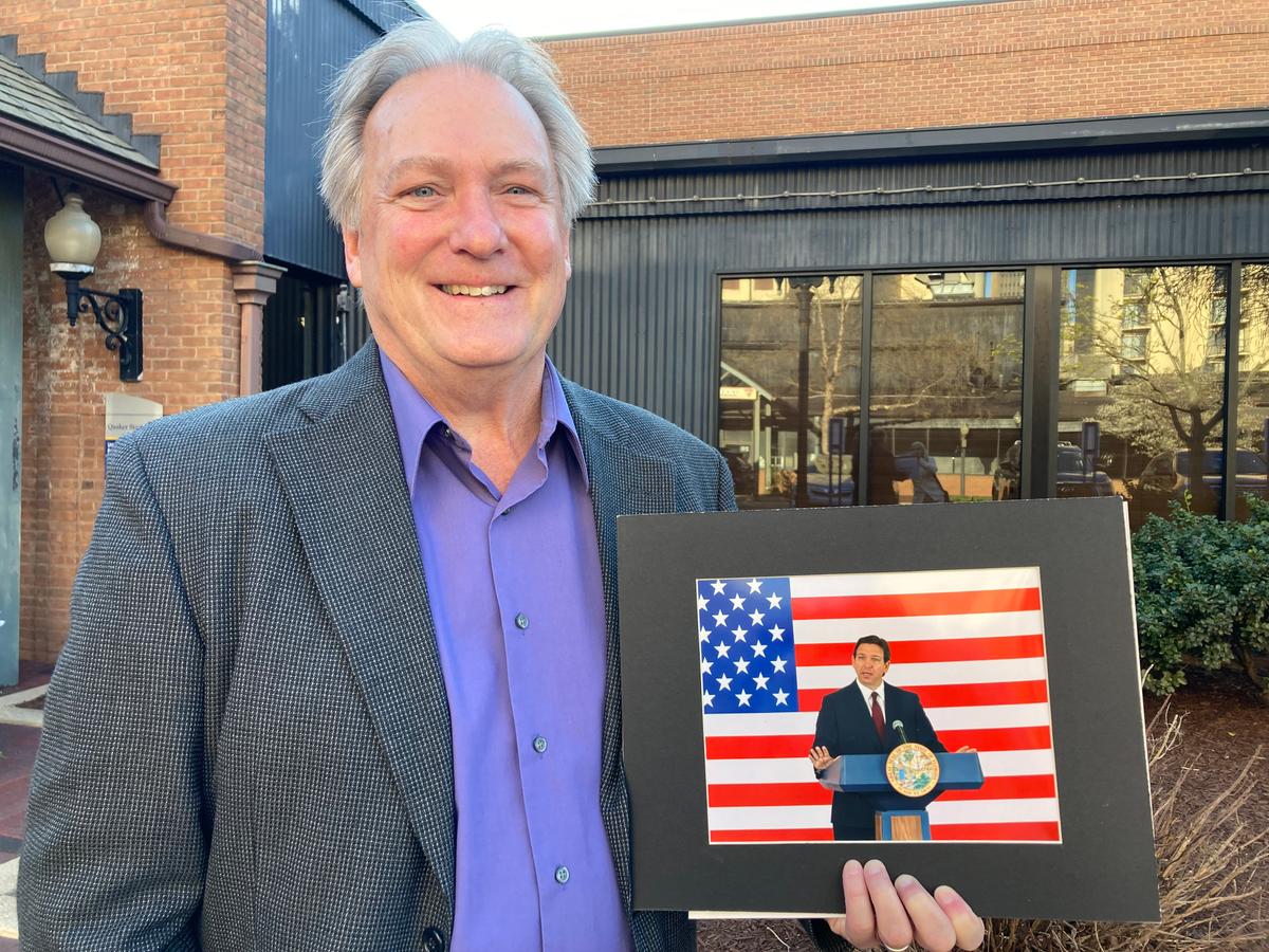 Dave Whitman poses with a photo of Florida Gov. Ron DeSantis. He is hoping to get DeSantis to sign it at an event in Akron, Ohio, on April 13, 2023. (Janice Hisle/The Epoch Times)