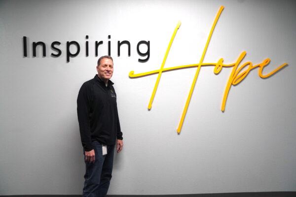 Thomas Bond, senior director of communications, marketing, and education, at Solari Crisis and Human Services in Tempe, Ariz., stands in front of a company sign on April 13, 2023. (Allan Stein/The Epoch Times)