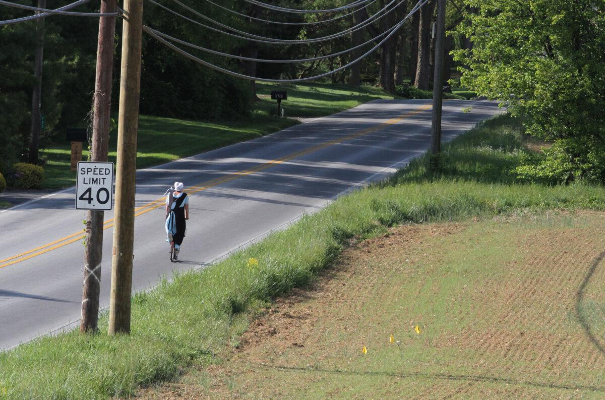 An Amish woman rides a scooter-like bicycle in Lancaster County, Pa., on April 26, 2023. (Richard Moore/The Epoch Times)
