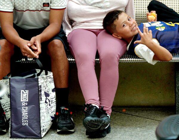 A young boy from Colombia waits for the bus with his parents in the Denver Reception Center on May 17, 2023. (Allan Stein/The Epoch Times)