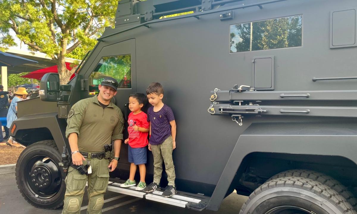 An Irvine SWAT officer poses with local children alongside his unit’s SWAT truck at the city's National Night Out at Woodbury Community Park in Irvine, Calif., on Aug. 1. (Carol Cassis/The Epoch Times)