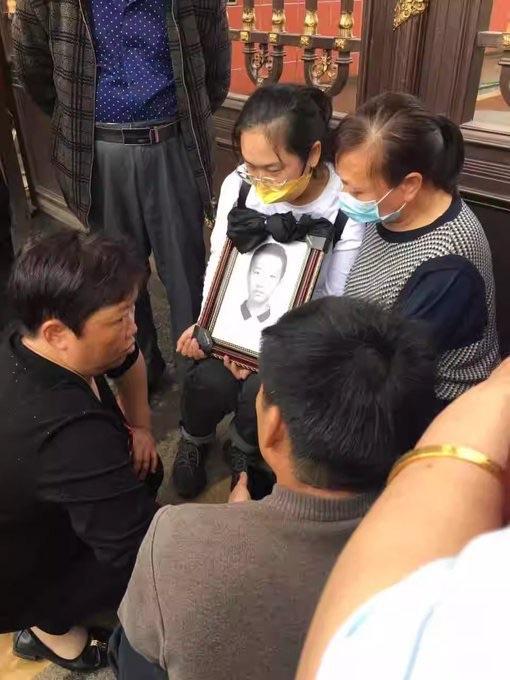 Parents holding up a portrait of their deceased loved one, a former student, in front of Zhongshan Vocational School in China's Hunan Province in May 2023. (Courtesy of Li Zhu)