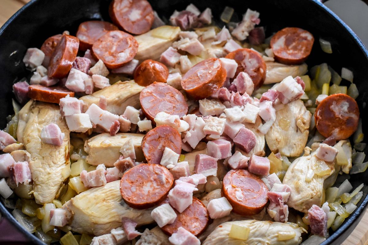 Cook the onions and garlic, then add chicken, chorizo, and pancetta until sizzling and fragrant. (Audrey Le Goff)