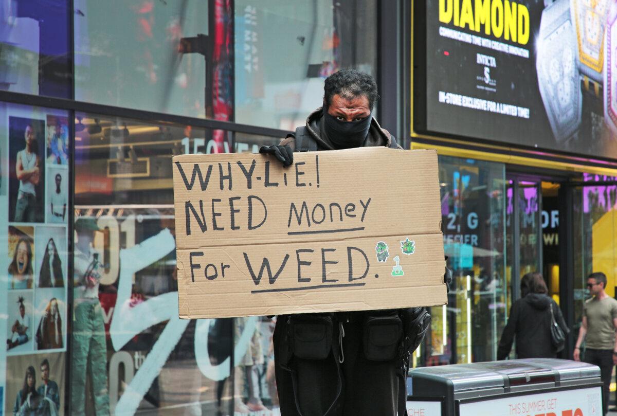 A man stands with a sign in New York's Times Square telling people he needs cash to buy marijuana on June 7, 2023. (Richard Moore/The Epoch Times)