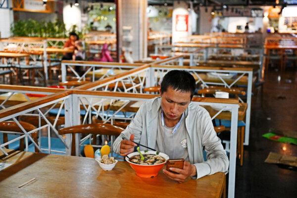 A man checks his phone while eating in a food court at a mall in Beijing on Aug. 15, 2023. (Greg Baker/AFP via Getty Images)