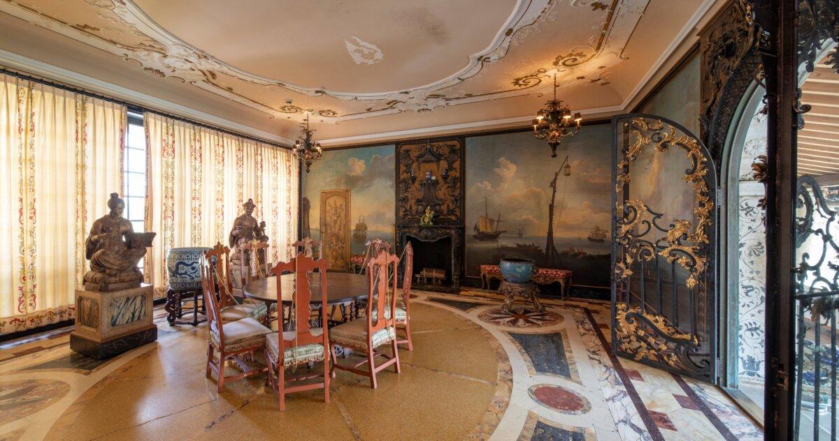 The second-floor breakfast room features an oval table that mirrors the inlaid, intricate marble floor design. Paintings on the walls by French artist Adrien Manglard (1695–1760) are divided into 11 panels showcasing a series of Italian harbor scenes. The rococo ornamental gate leads to the courtyard. When Vizcaya was built, the curated gates were retrofitted to fit their selected openings. (Robin Hill/Vizcaya Museum and Gardens)
