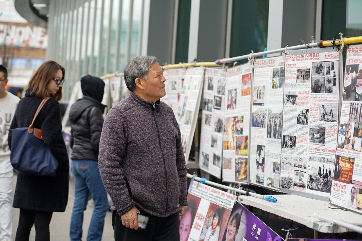 Bystanders look at a display board in front of a Falun Gong booth, in the Flushing neighborhood of Queens, New York, on April 21, 2024. (Chung I Ho/The Epoch Times)