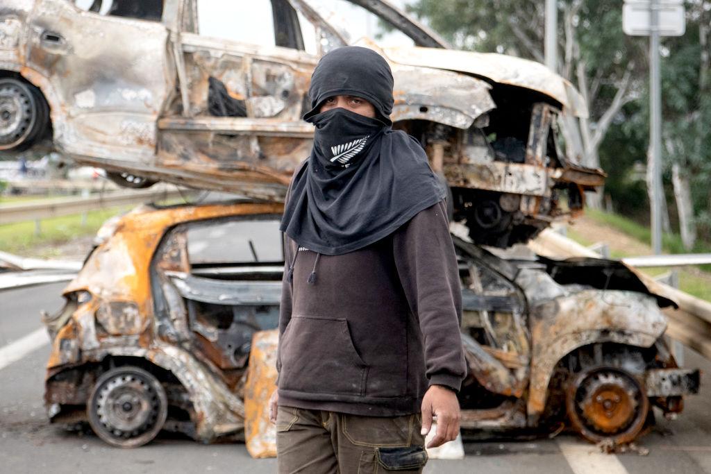 A bystander in front of burnt vehicles in a roadblock at the entrance to Ducos, France's Pacific territory of New Caledonia, on May 21, 2024. The Pacific territory of 270,000 people has been in turmoil since May 13, when violence erupted over French plans to impose new voting rules that would give tens of thousands of non-indigenous residents voting rights. (Delphine Mayeur/AFP via Getty Images)