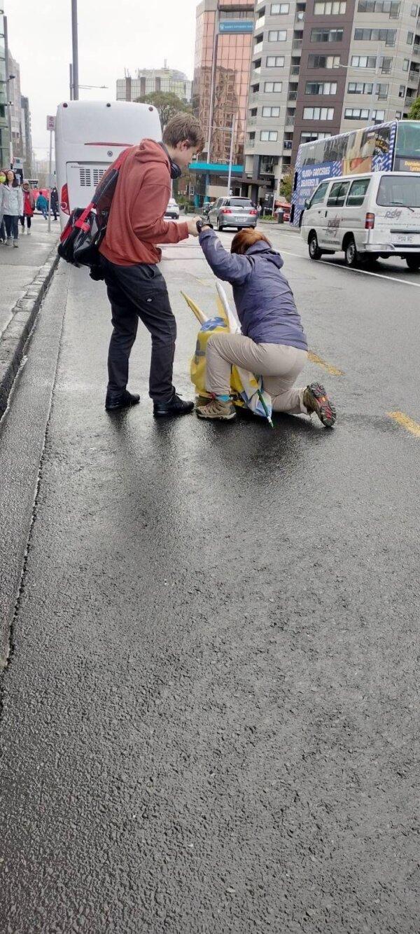 A passenger helped a female Falun Gong practitioner who was pushed to the road by a pro-Beijing protester in Auckland, New Zealand, on June 14, 2024. (Supplied)