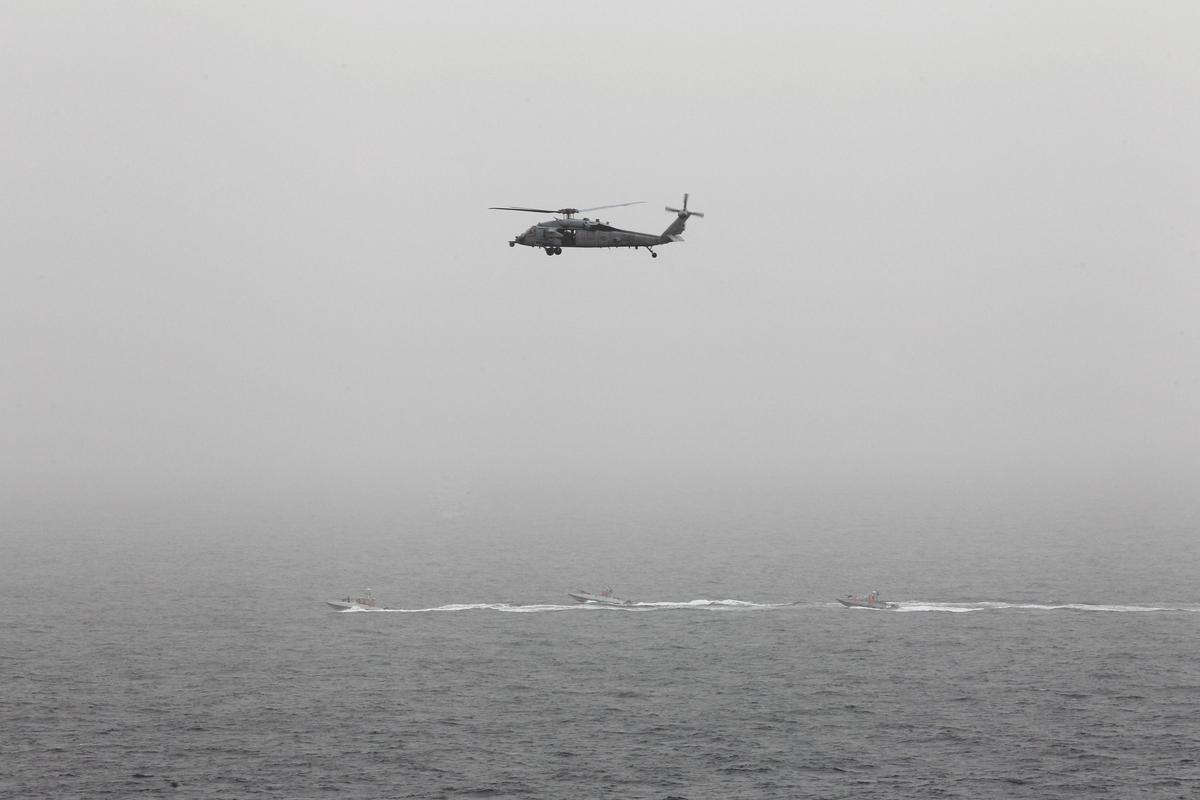 Three Iranian Revolutionary Guard boats are seen near the U.S. aircraft carrier, USS George H. W. Bush while transiting Straits of Hormuz as U.S. Navy helicopter hovers over them during early hours of March 21, 2017. (REUTERS/Hamad I Mohammed)