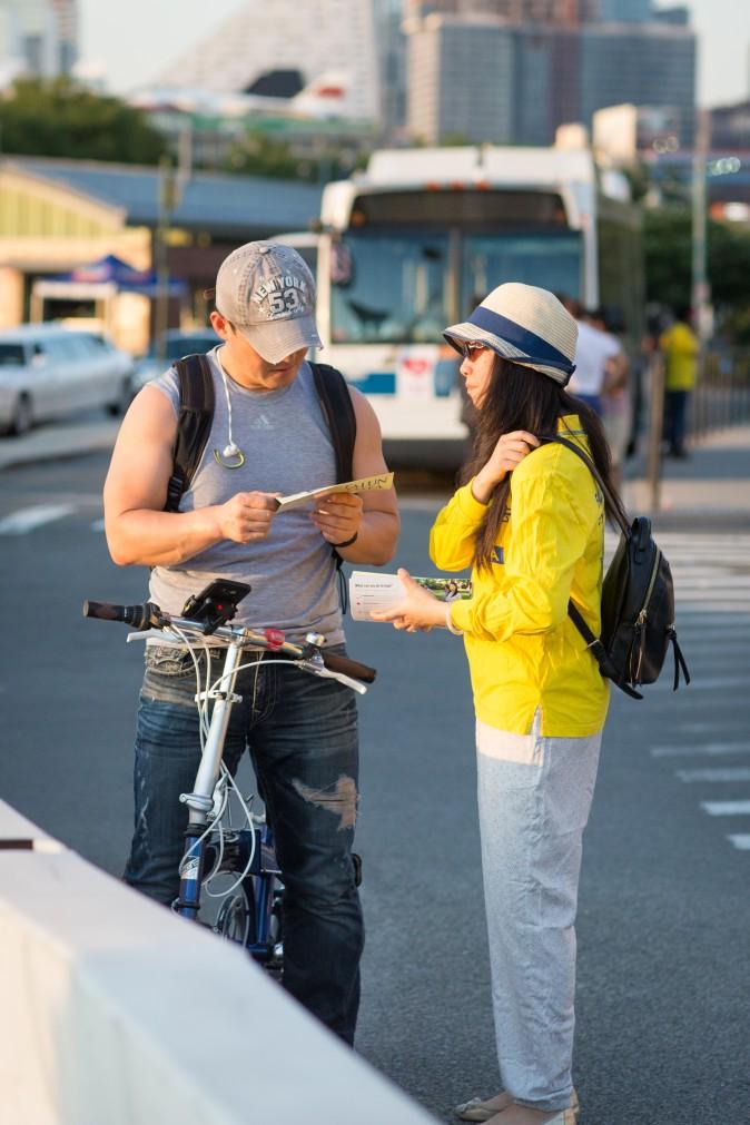 A Falun Gong practitioner hands out pamphlets about the practice and the Chinese regime's persecution campaign to a passerby near the Chinese Consulate in New York on July 16, 2017.  (Benjamin Chasteen/The Epoch Times)