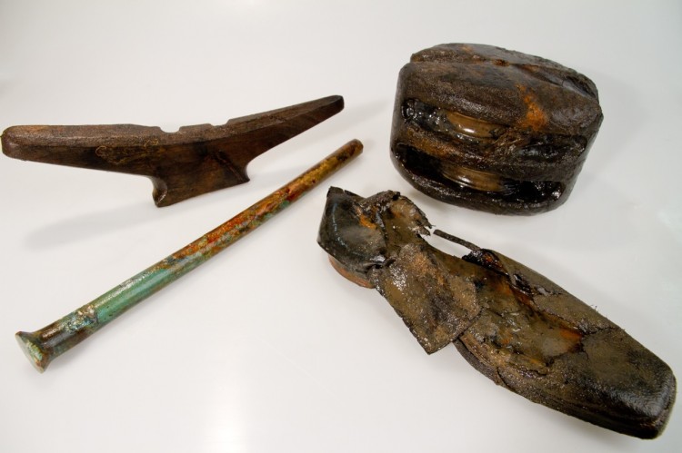 Artifacts recovered from HMS Investigator, from left to right: a wooden horn cleat, which the ropes would have been looped around for tying the vessel's rigging, a copper alloy bolt used to fasten ship timbers, a leather shoe, and a double-sheave pulley (Louis Barnes/Parks Canada )