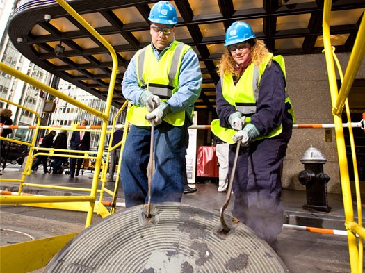 Two Con Edison workers lift a manhole cover in front of the Radio City Music Hall in Manhattan on September 27, 2011. (Courtesy of Con Edison)