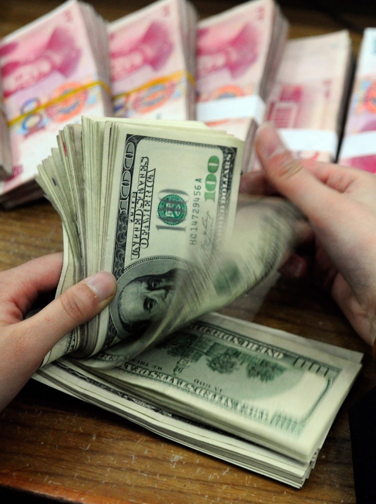 CHINA FOREX: A Chinese bank worker counts a stack of U.S. dollars together with stacks of 100 Chinese yuan notes. China is driving up its national debt to finance its foreign currency reserves, the largest in the world.  (STR/AFP/Getty Images)