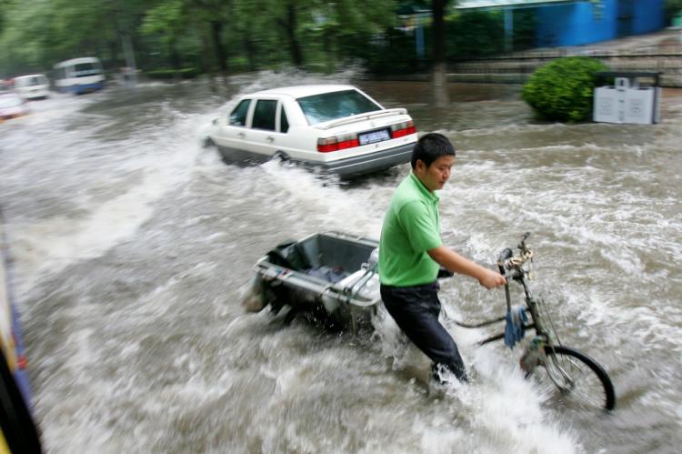 ALL WET: A man pushes a tricycle along a flooded road after heavy rain on August 10, 2008 in Beijing, China. (China Photos/Getty Images)