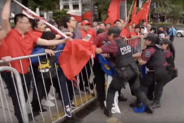 Um participante do grupo pró-Pequim ataca um praticante do Falun Gong com um mastro de bandeira (Captura de tela via YouTube)