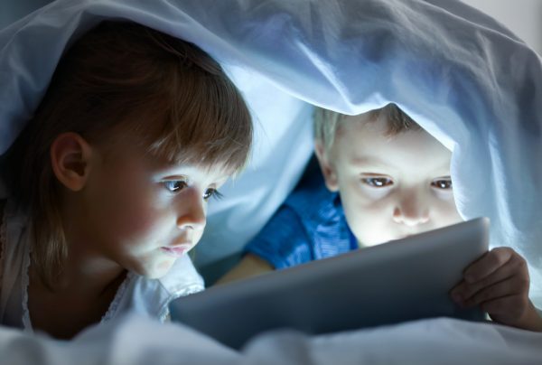 children lying under blanket with tablet